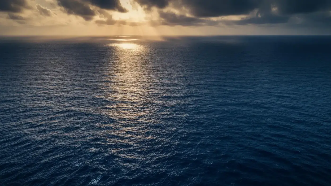 Aerial view of a vast deep blue ocean with sunlight on the surface